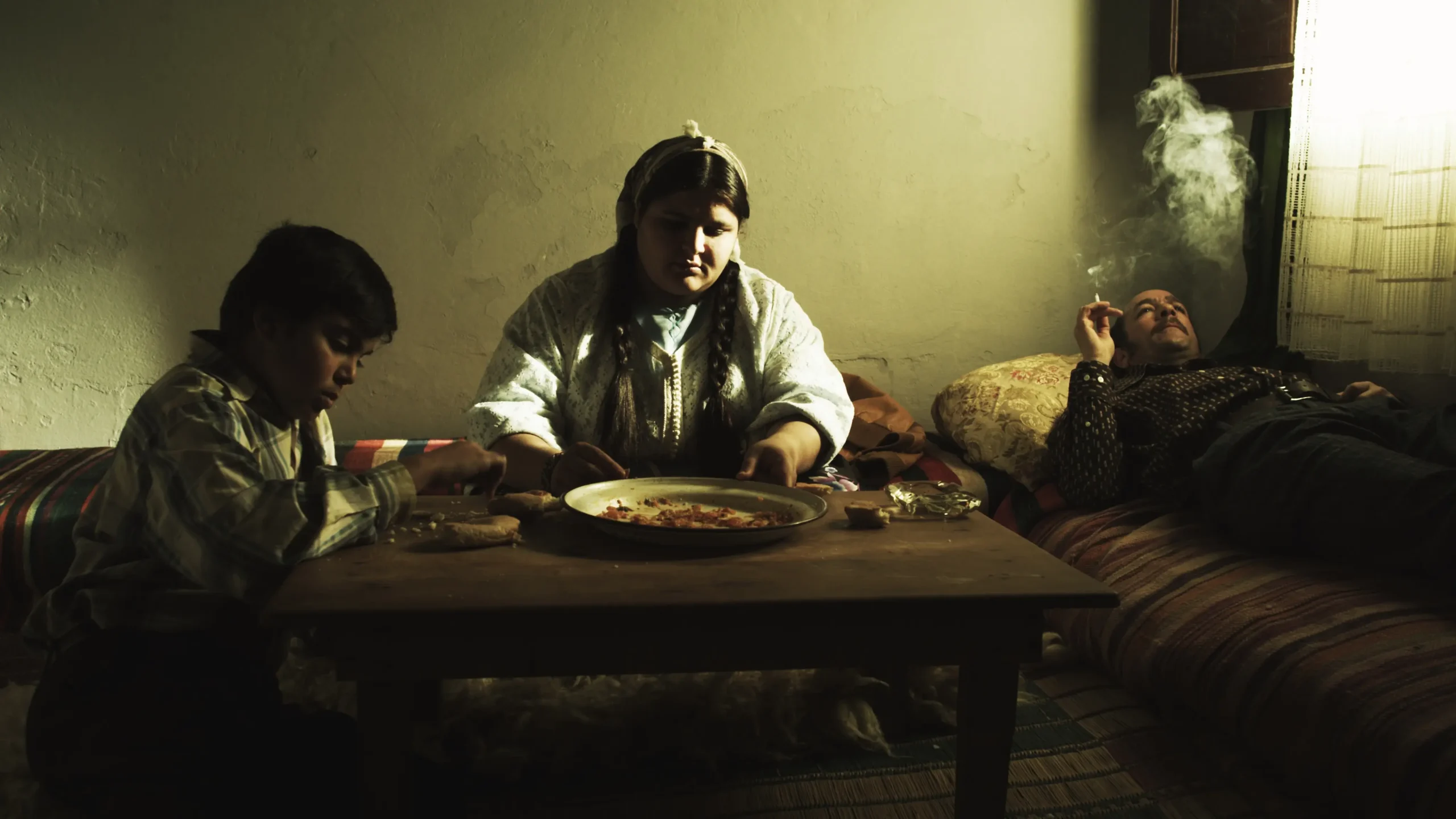 A promotional still from Adios Carmen showing three people gathered around a low table